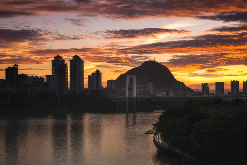 城市上空的夕阳或日出 背景是湖泊或河流 山脉在远处。