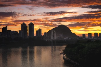 城市上空的夕阳或日出 背景是湖泊或河流 山脉在远处。