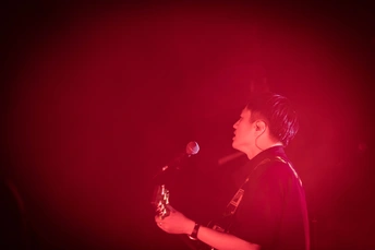 一名男子在晚上红灯的舞台上演奏乐器 站在麦克风前 一名男子对着乐器唱歌