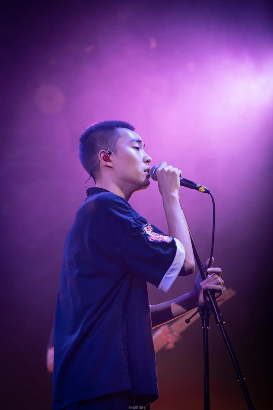 一个拿着麦克风的年轻人站在舞台上表演歌曲的人面前