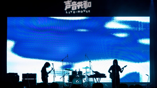 舞台上有一支乐队在大型屏幕前为一大群人表演