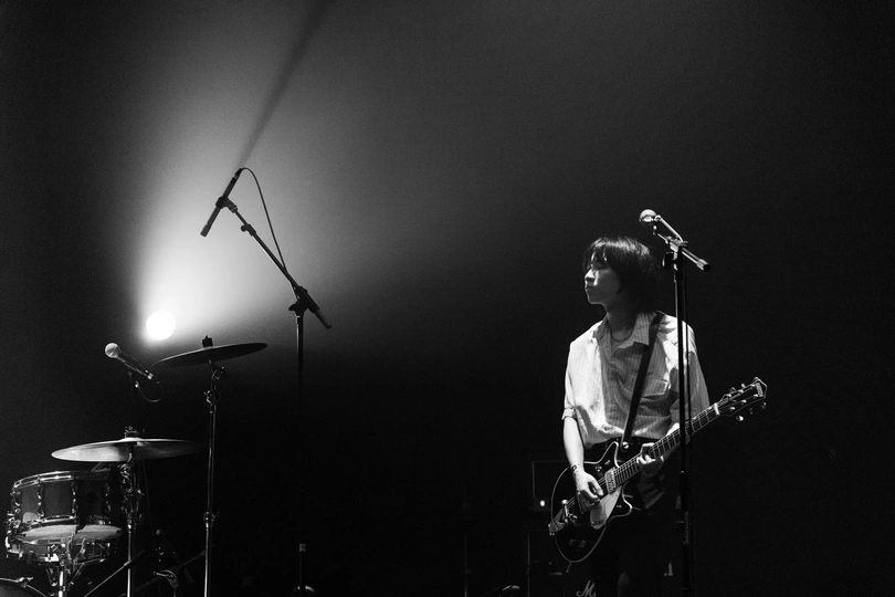 一个黑白图像 描绘一个人在夜晚的舞台上演奏乐器 手持麦克风 乐队正在表演。