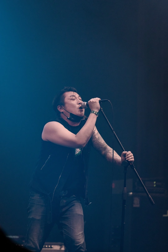 一个在舞台上唱歌对着麦克风的男人 背景有乐队演奏。