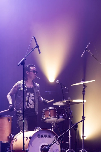 一个在舞台上弹鼓的男子 背景有一支乐队在表演。