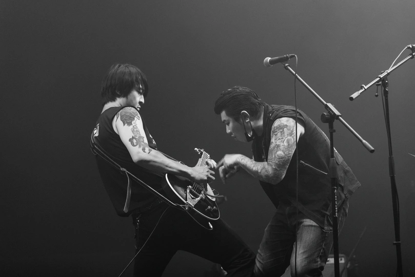 一张乐队在演唱会上表演的舞台上表演的照片 乐队成员正在弹吉他并对着话筒唱歌。