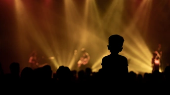 一个男孩站在舞台前 周围有一群人参加音乐会 形成剪影。