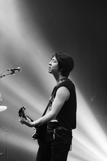 一个黑白图像 展示一个男子在夜晚的舞台上弹奏乐器 手持麦克风 旁边还有一个人站着。