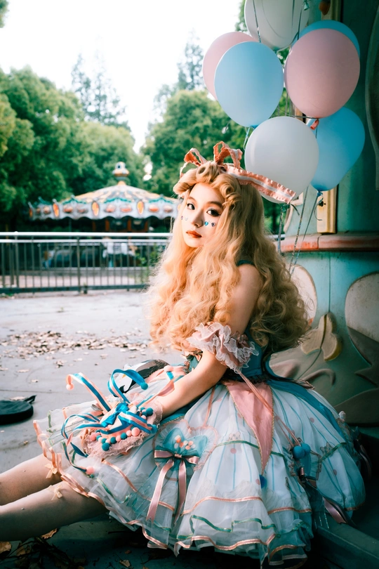 一个穿粉红色裙子的女人坐在地上 周围有蓝色气球。