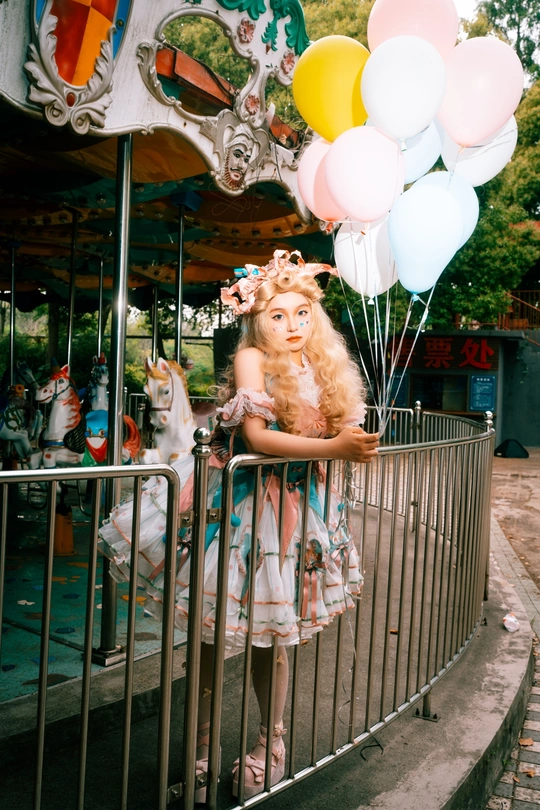 一个小女孩穿着粉色裙子 拿着气球站在马戏团旁边。