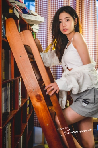 一位年轻女子靠在一根木梯上 木梯靠在书架旁 在图书馆里。