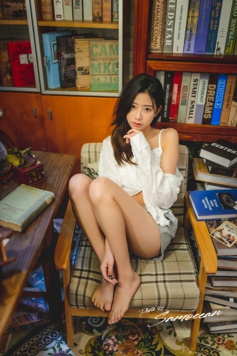 一个年轻女子坐在椅子上 双腿交叉在书架前。