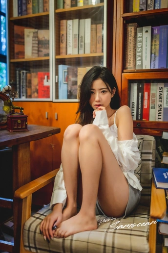 一个年轻女子坐在图书馆的一把椅子上 双腿交叉 身后有书架。