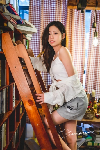 一个年轻女子坐在有书架的房间里 正在爬木梯子。