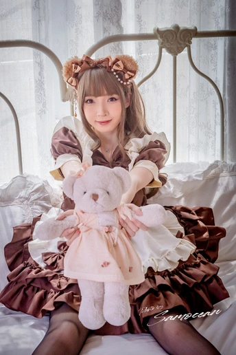 一个穿着粉红色连衣裙的小女孩抱着一只小毛绒玩具坐在床上