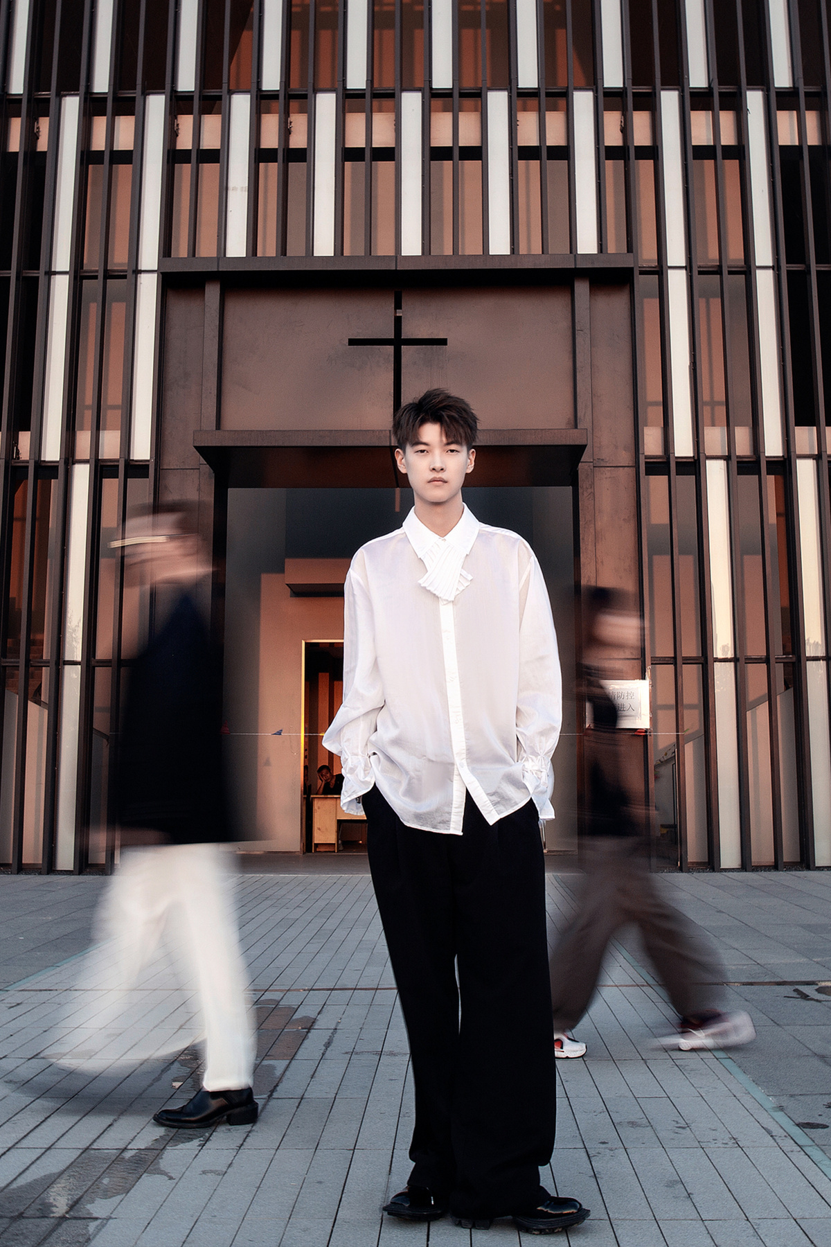 一个穿着白衬衫、打着黑领带的年轻人站在一栋楼前的人行道上