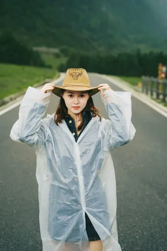 一位穿着雨衣和帽子站在公路中央的年轻女子