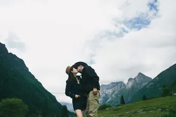 一个男人在山上吻着一个站在山丘上的女人 背景是山脉。