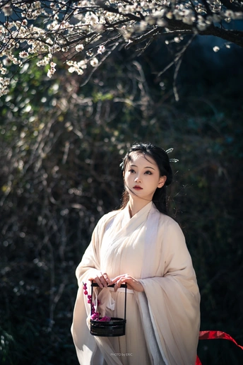 一位穿着传统白色和服的美女站在盛开的花树下