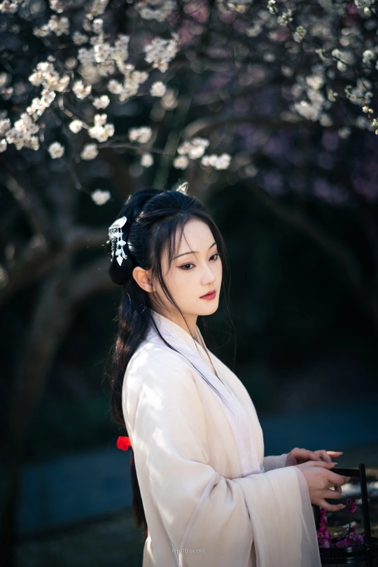 一位穿着传统白色裙子的女人站在一朵盛开的树下