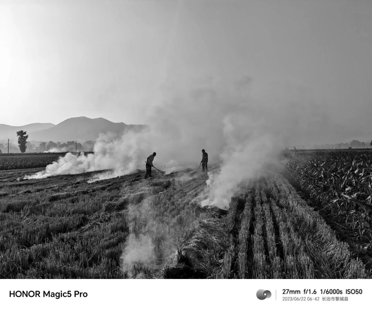一张黑白照片 农民站在一个有烟冒出的田地里