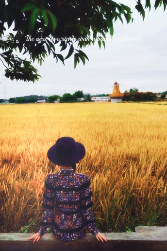 一个人坐在长凳上 正在看麦田 中间站着一个戴帽子的小女孩。