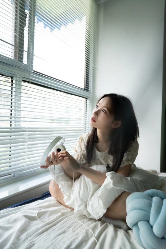 一个年轻女子坐在白色床上 凝视着窗外。