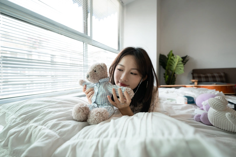 一个年轻女子抱着一只泰迪熊坐在床上端着一杯东西