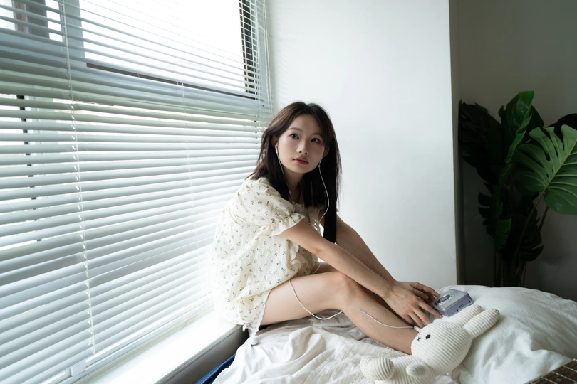 一个年轻女子坐在靠近窗户的白床上