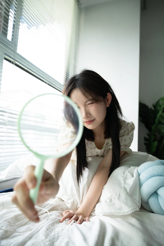 一个年轻女子躺在床上 透过放大镜看书。