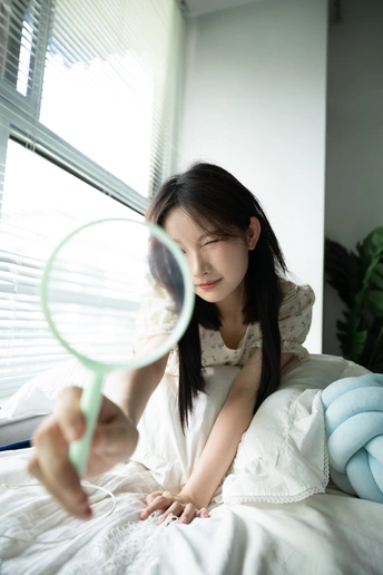 一个年轻女子躺在床上 透过放大镜看书。