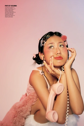 一位身穿粉色连衣裙、化着妆的年轻女子把一部粉色电话放在耳边