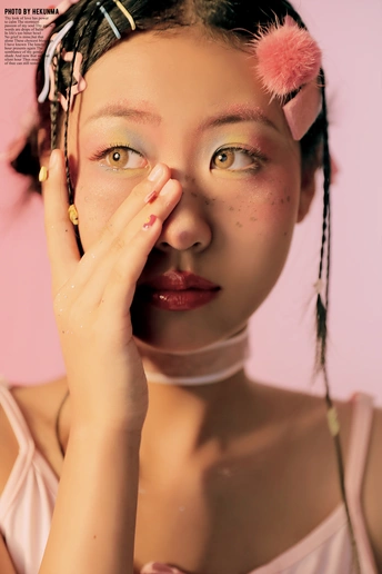 一位粉红色头发、化着妆的年轻女子在杂志前摆姿势