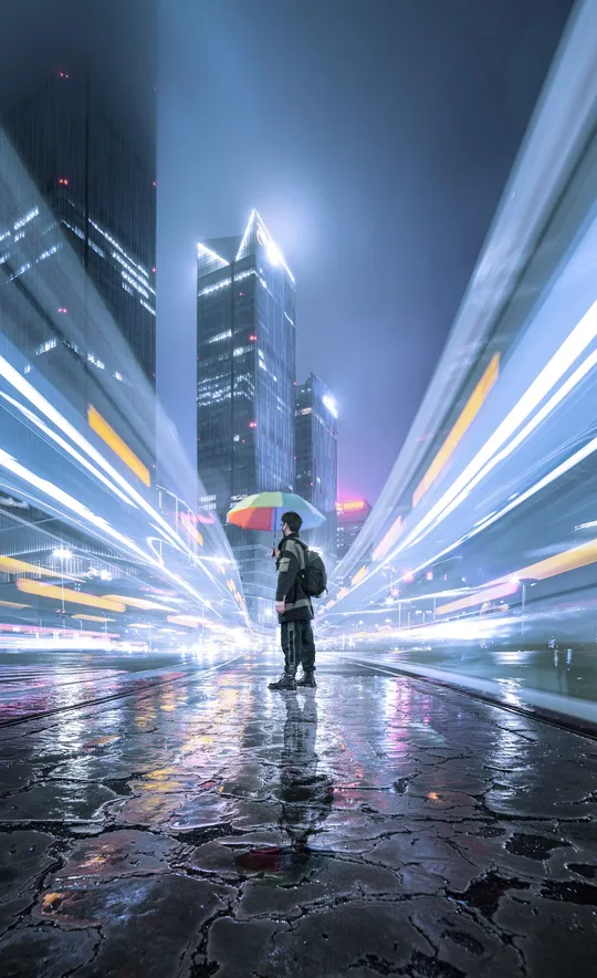 在雨中站着的男人 带着伞 在一个雨夜的城市中。