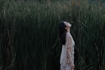 一个穿着连衣裙的年轻女子站在水边一片高高的草地上
