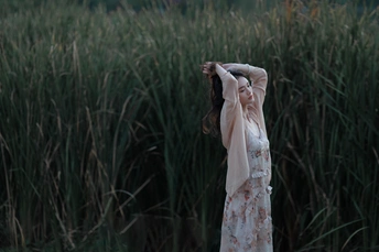 在一片高高的草地上 一位身穿白色连衣裙的年轻女子将伞举过头顶