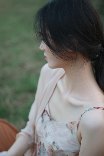 一个穿着连衣裙的年轻女子坐在草地上抓着头发