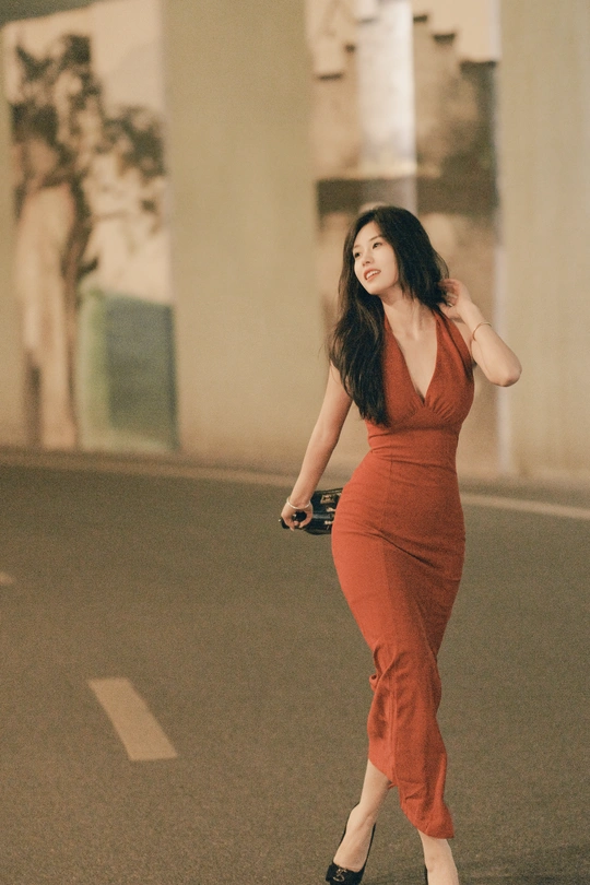 一位穿着橙色连衣裙的年轻女子走在一条空荡荡的街道上。