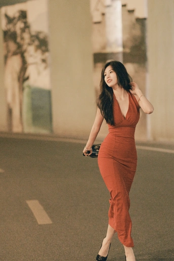 一位穿着橙色连衣裙的年轻女子走在一条空荡荡的街道上。