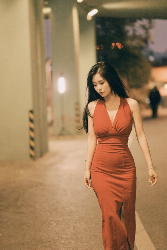 一个穿着橙色连衣裙的年轻女子在夜晚走下空荡荡的街道