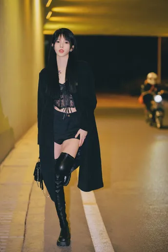 一位穿着黑色外套和高筒靴子的女孩在街上。