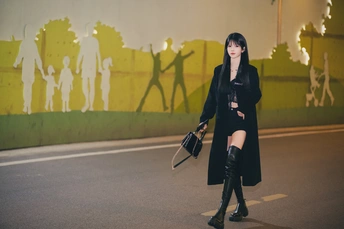 一位穿着黑色外套和靴子的年轻女子正在街上走。