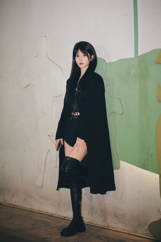 一位穿着长款外套和黑色靴子的年轻女子站在一面墙前