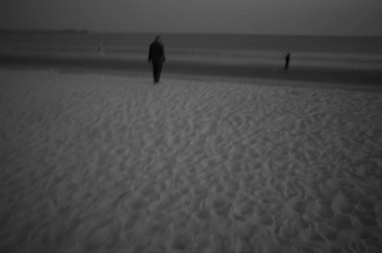 一个黑白海滩 人们在沙滩上走 一个人站在水里。