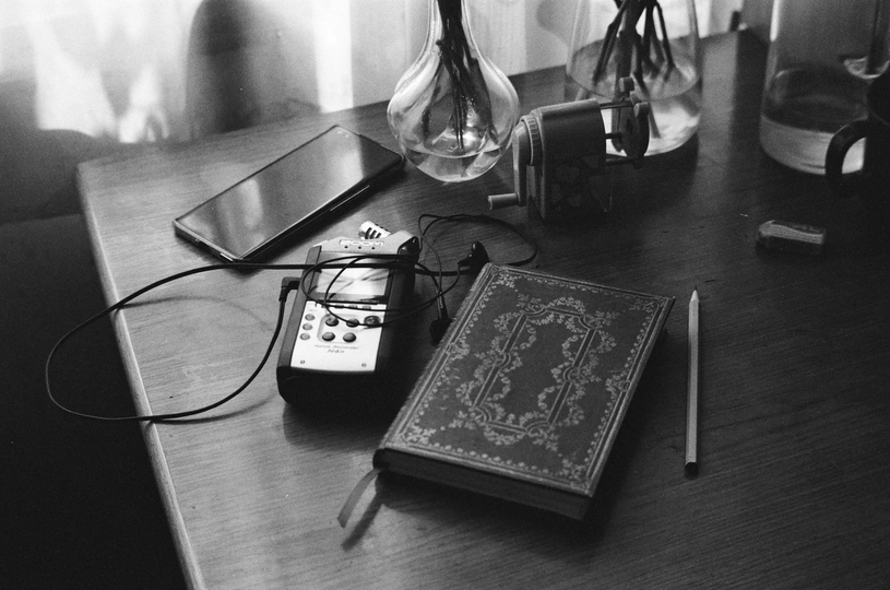 一个木制桌子 上面放着一本书、遥控器、钢笔、笔记本和一部手机。