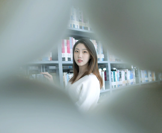 一位年轻女子站在图书馆的书架前看着镜子
