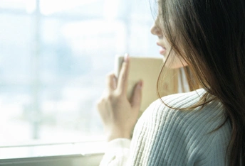 一个年轻女子拿着一本书望着窗外
