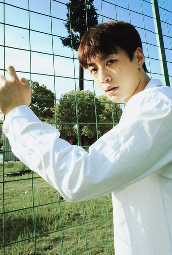 一个穿着白衬衫的年轻人伸出双臂靠在铁丝网上 一只长颈鹿站在他身后的围栏里