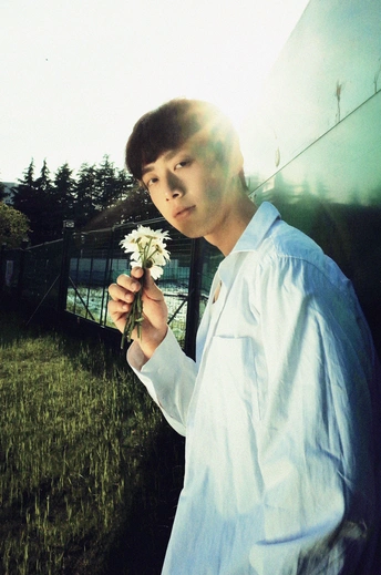 一个穿着白衬衫的年轻人手里拿着一朵花站在田野里