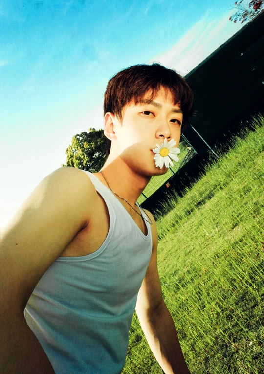 一个穿着白色背心的年轻人站在田里 嘴里叼着一朵白花