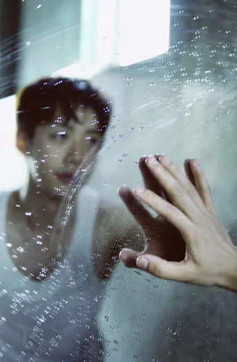 一个男人透过有水溅在上的窗户 一个女人透过玻璃看。